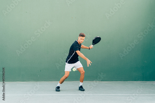 Man playing paddle tennis on an outdoor green paddle tennis court at the sunset © Henko Studio