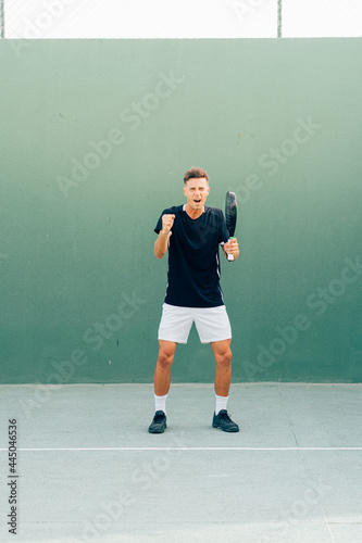 Paddle tennis player celebrating victory at the end of the match on the green court at sunset