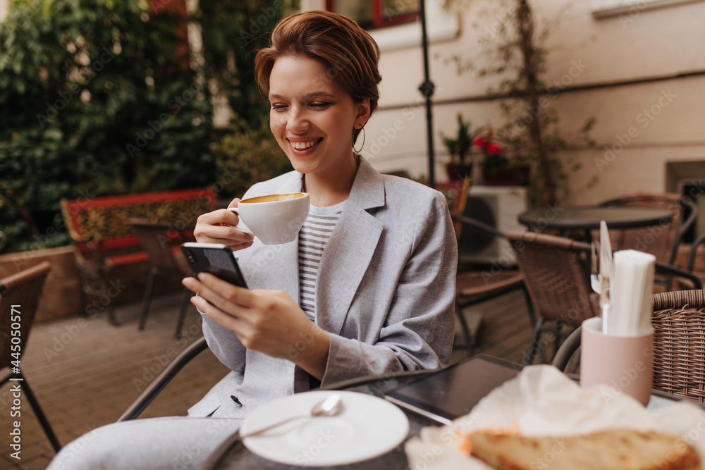 Fototapeta Woman chatting on smartphone and drinking coffee