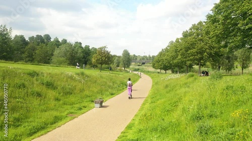 Woman riding electric scooter on park path into footage, static shot