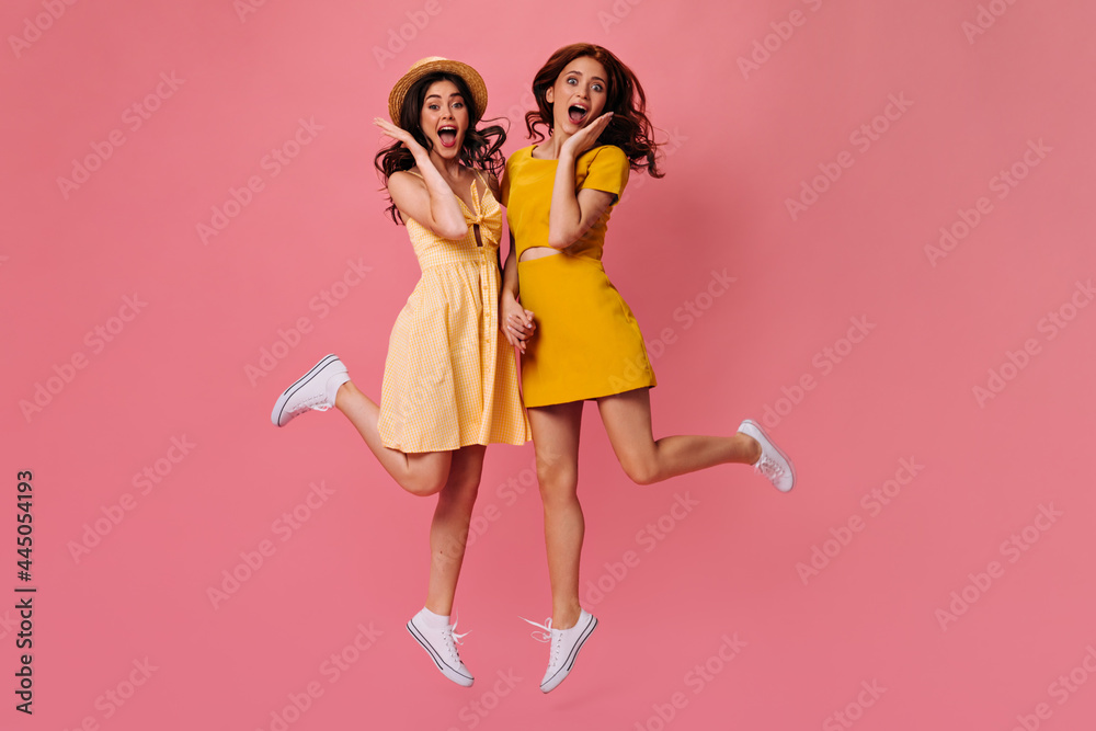 Surprised ladies in yellow dresses jumping on isolated background. Curly-haired girlfriends in cute short dresses posing and holding hands Surprised ladies in yellow dresses jumping on isolated background. Curly-haired girlfriends in cute short dresses posing and holding hands