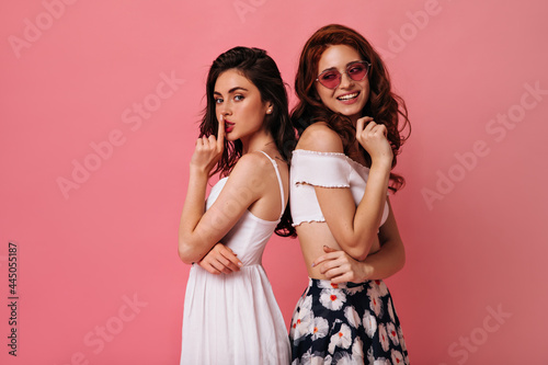 Ladies in good humor pose on isolated background. Wonderful women with dark hair in fashionable clothes smile on camera