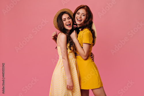 Girls in yellow dresses smiling on pink background. Lovely young women in summer light clothes cheerfully posing for camera