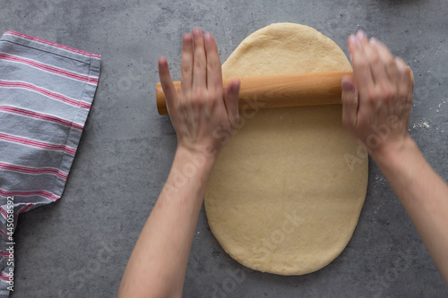 Dough flatten by white blurred woman hands using a rolling pin on a rustic gray table.