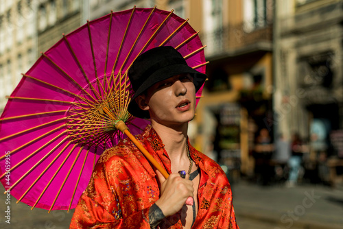 Positive man portrait with dressed in street style clothes red kimono with chains around neck with pink umbrella. Youth and lifestyle concept. Luxury rap artist.