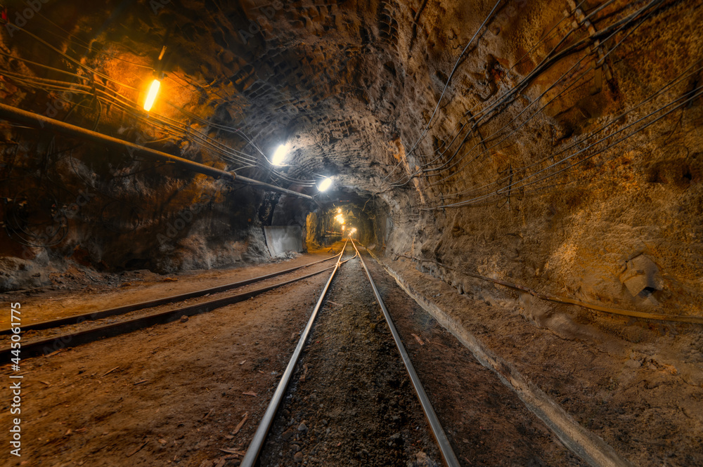 Naklejka premium Tunnel of the mining of an underground mine. Lots of pipelines on the ceiling and rail track for trolleys