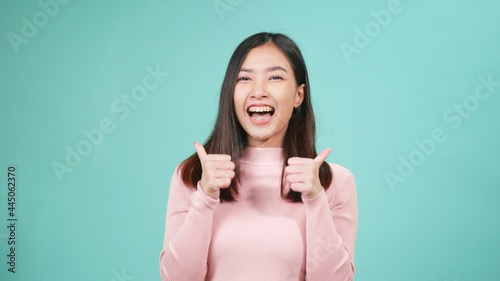 Portrait young Asian happy beautiful woman smiling wear silicone orthodontic retainers on teeth showing thumb up finger isolated on blue background. Dental hygiene and health concept