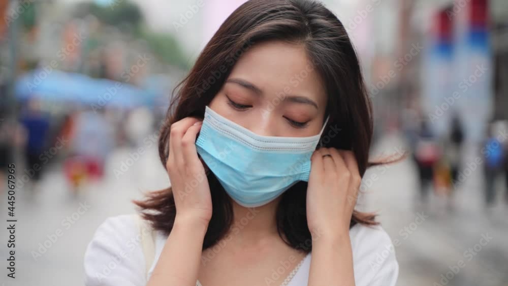 asian woman take off mask looking at camera smile in the urban asian street  The epidemic of Covid-19 is over happy people remove mask enjoy the life