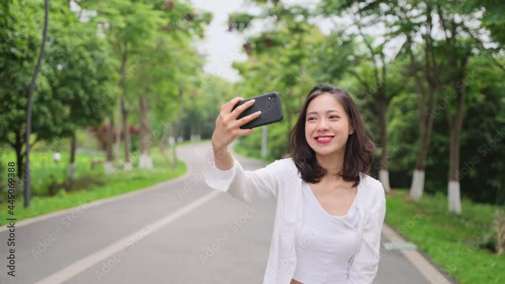 slow motion of pretty young asian woman walking in the summer park looking at moble phone video chatting smile relax joyful girl walking on the road slow motion of pretty young asian woman walking in the summer park looking at moble phone video chatting smile relax joyful girl walking on the road