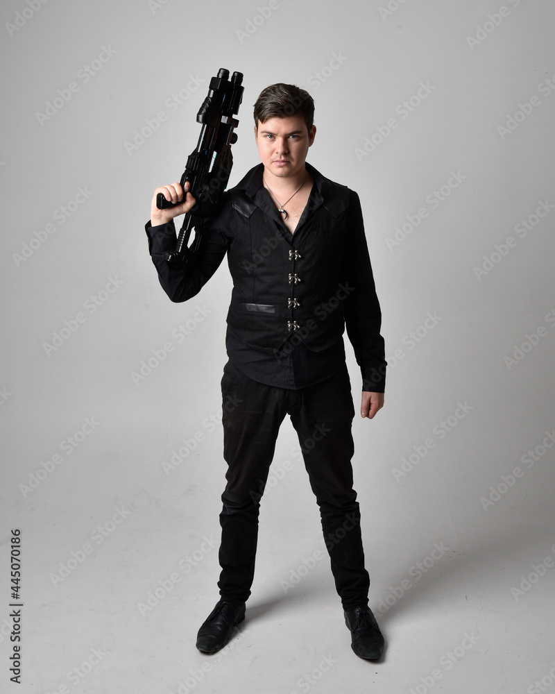 Full length portrait of a brunette man wearing leather jacket and holding a science fiction gun. Standing action pose isolated against a grey studio background. Full length portrait of a brunette man wearing leather jacket and holding a science fiction gun. Standing action pose isolated against a grey studio background.
