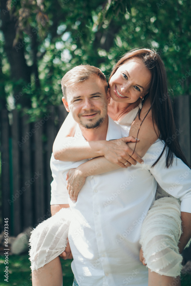 Fototapeta premium the love of a young husband and wife, happy faces, a date in nature, joy, a guy rides a girl on his back. Love forever Romance young
