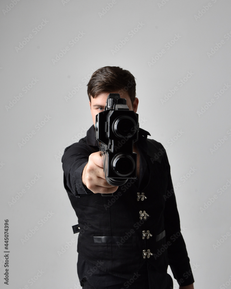 Obraz premium close up portrait of a brunette man wearing leather jacket and holding a science fiction gun. action pose isolated against a grey studio background.