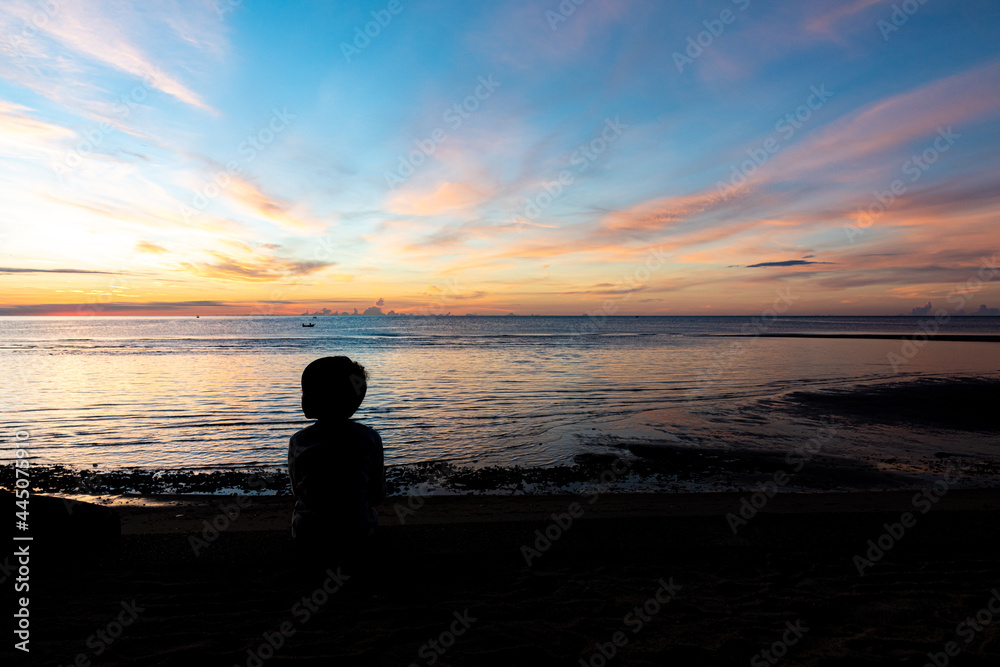 the boy silhouette on a sea beach at sunrise, kid and sea