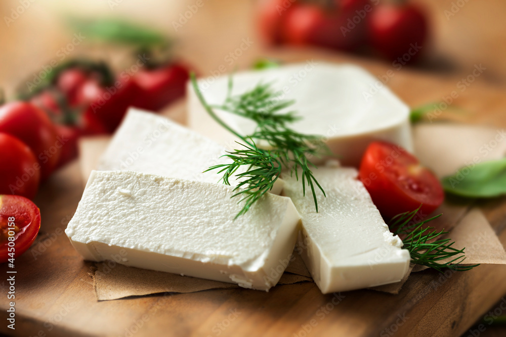 Feta cheese with dill and cherry tomatoes on cutting board close up