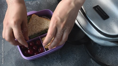 Women hands puts in lunch box with a sandwich, cookies and cherries from a backpack. Concept of a snack at school, office, outside the home.