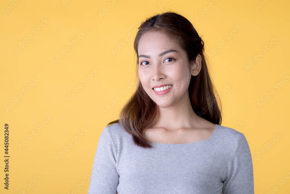 Obraz premium Portrait of a beautiful smiling young Asian woman in casual clothes standing isolated over yellow background, looking at camera