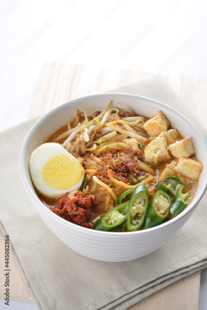 Malay mee rebus noodle with boiled egg, tofu, green chilli, sambal chilli sauce and hot thick curry gravy soup bowl in white background asian halal menu Malay mee rebus noodle with boiled egg, tofu, green chilli, sambal chilli sauce and hot thick curry gravy soup bowl in white background asian halal menu