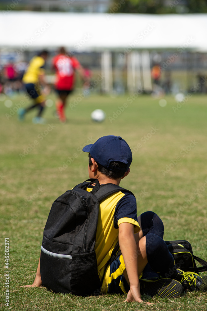 Junior soccer player rests with his teammates on a sideline waiting for their next match in a football school tournament, while some pitches still in action. Junior soccer player rests with his teammates on a sideline waiting for their next match in a football school tournament, while some pitches still in action.