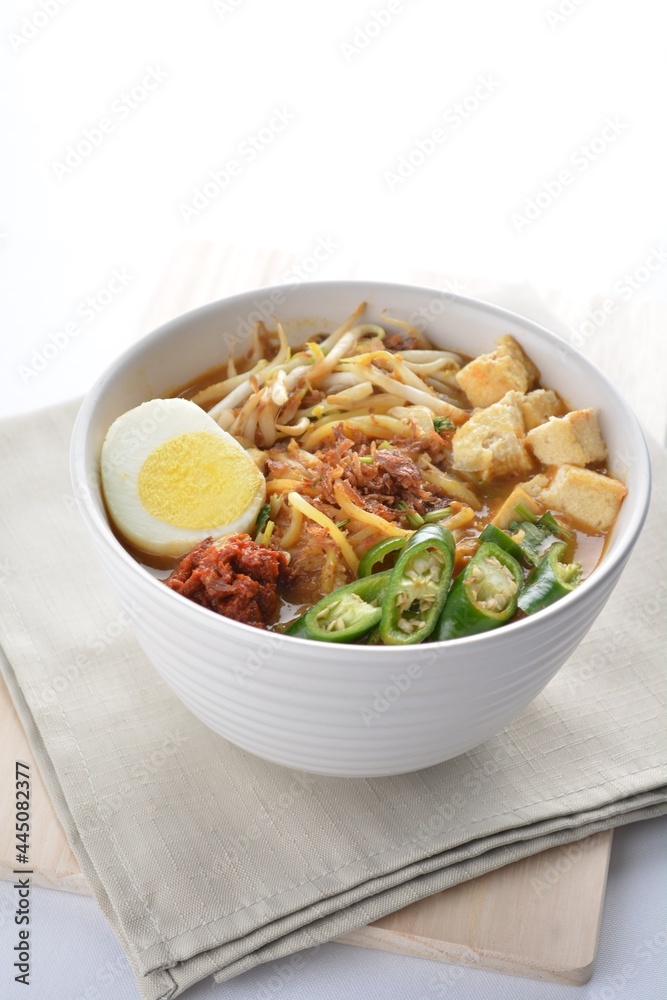 Malay mee rebus noodle with boiled egg, tofu, green chilli, sambal chilli sauce and hot thick curry gravy soup bowl in white background asian halal menu Malay mee rebus noodle with boiled egg, tofu, green chilli, sambal chilli sauce and hot thick curry gravy soup bowl in white background asian halal menu