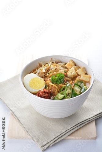 Malay mee rebus noodle with boiled egg, tofu, green chilli, sambal chilli sauce and hot thick curry gravy soup bowl in white background asian halal menu