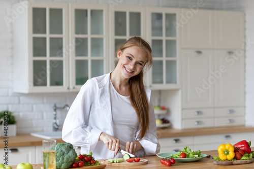 Beautiful happy woman in the kitchen preparing vegetable salad smiling looking at the camera.