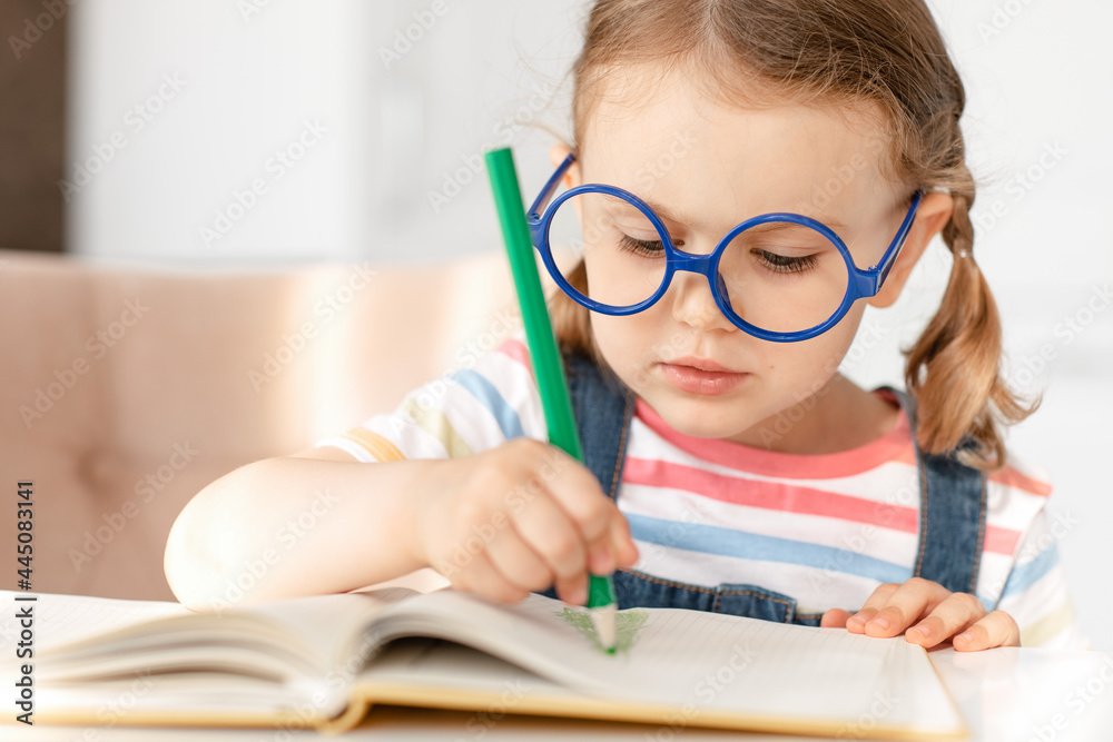 Smart child girl with glasses draws colored pencils at table in white kitchen. Developing children's skills, kid hobbies, education and learning, back to school. Background, copy space Smart child girl with glasses draws colored pencils at table in white kitchen. Developing children's skills, kid hobbies, education and learning, back to school. Background, copy space