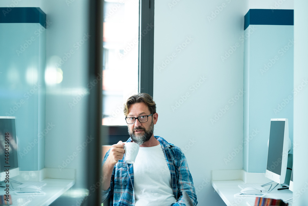 Fototapeta premium Mature man portrait looking on camera while drink coffee at office - freelance online job with computer concept lifestyle - adult caucasian people in coworking space - blue mood colors modern people