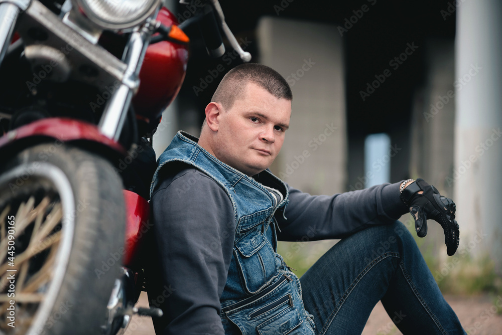 A tired motorbiker sits on the ground near the motorcycle.