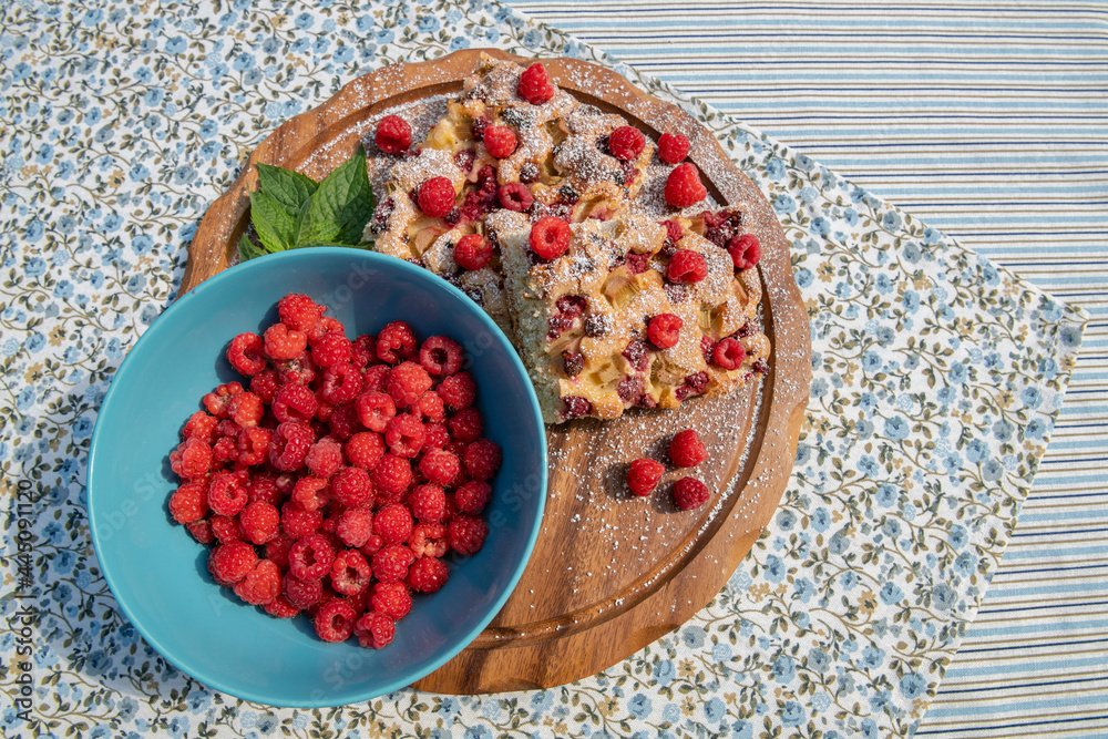 Bowl with fresh raspberries, and pie with raspberries and rhubarb on the wooden board