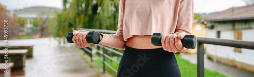 Unrecognizable young woman training with dumbbells outdoors