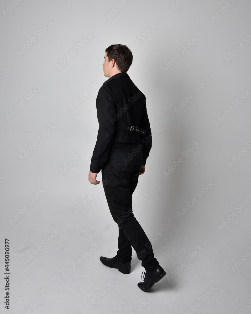 Full length portrait of a brunette man wearing black shirt and gothic waistcoat. Standing pose isolated against a grey studio background. Full length portrait of a brunette man wearing black shirt and gothic waistcoat. Standing pose isolated against a grey studio background.