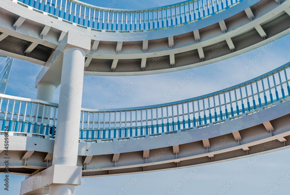 Two parts of a circular ramp of pedestrian bridge with blue cloudy sky ...