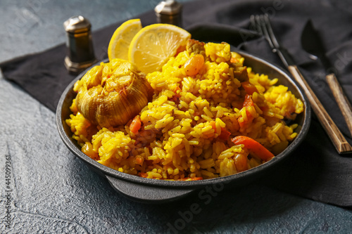 Frying pan with tasty pilaf on dark background