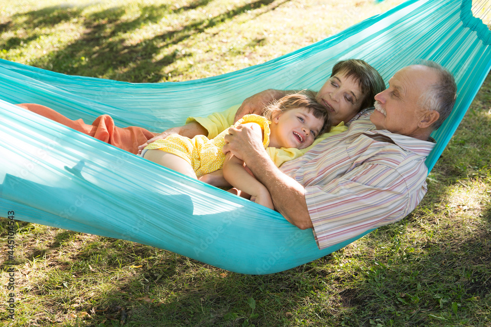Little child girl with grandparents lie in a hammock in a summer park or garden. Concept of friendly family.
