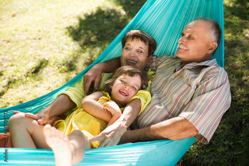 Little child girl with grandparents lie in a hammock in a summer park or garden. Concept of friendly family.
