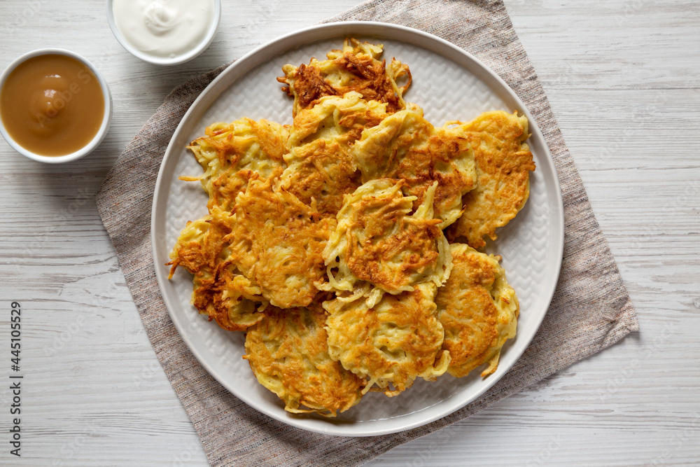 Homemade Potato Pancakes Latkes with Apple Sauce and Sour Cream on a white wooden surface, top view. Flat lay, overhead, from above. Homemade Potato Pancakes Latkes with Apple Sauce and Sour Cream on a white wooden surface, top view. Flat lay, overhead, from above.