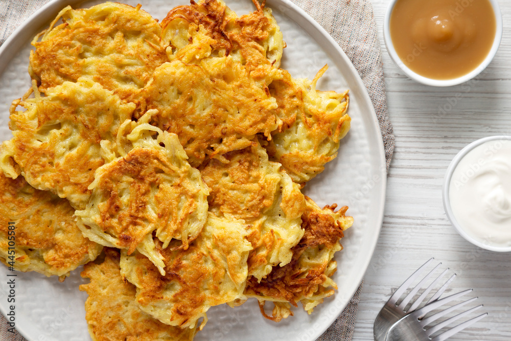 Homemade Potato Pancakes Latkes with Apple Sauce and Sour Cream on a white wooden background, top view. Flat lay, overhead, from above. Homemade Potato Pancakes Latkes with Apple Sauce and Sour Cream on a white wooden background, top view. Flat lay, overhead, from above.