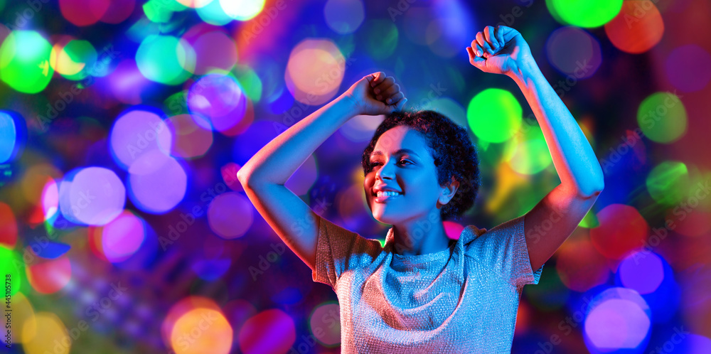 Fototapeta premium leisure, clubbing and nightlife concept - smiling young african american woman dancing in ultraviolet neon lights over bokeh background