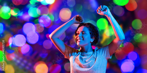 leisure, clubbing and nightlife concept - smiling young african american woman dancing in ultraviolet neon lights over bokeh background