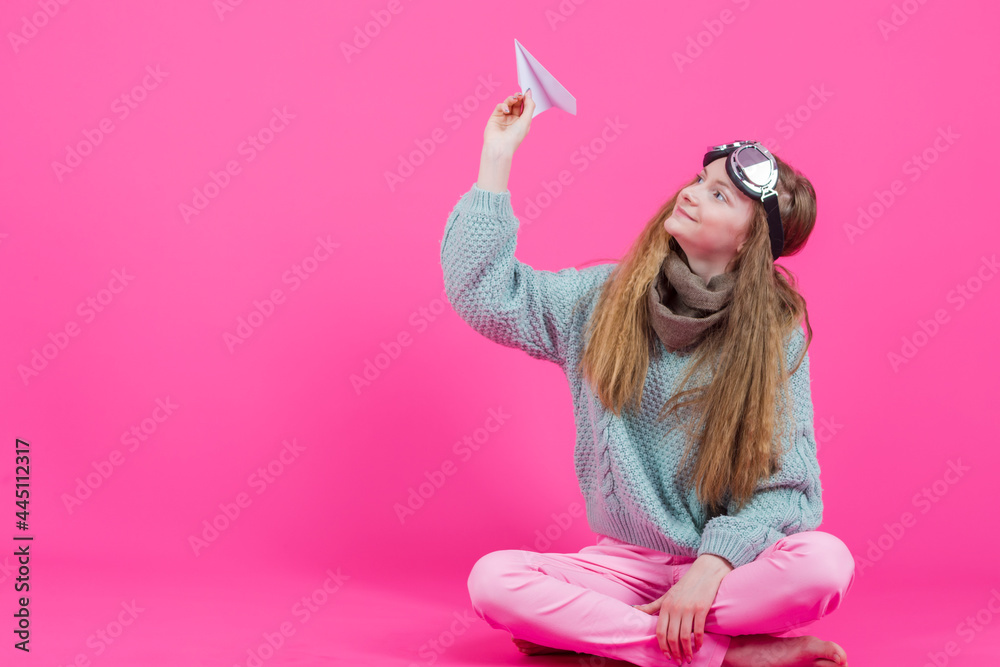 Smiling Caucasian Teenage Girl in Flying Glasses and Knitted Sweater Launching Origami Paper Plane While Posing Over Pink Background.