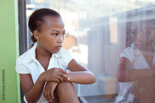 African american schoolgirl sitting in school classroom looking out of window © wavebreak3