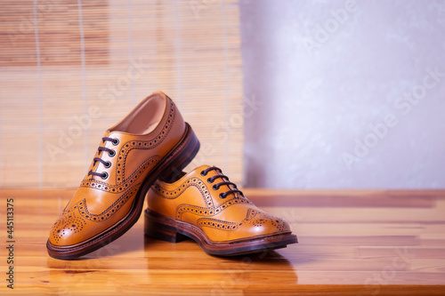 Pair of Full Broggued Tan Leather Oxfords Broggued Shoes Against White Wall Background.