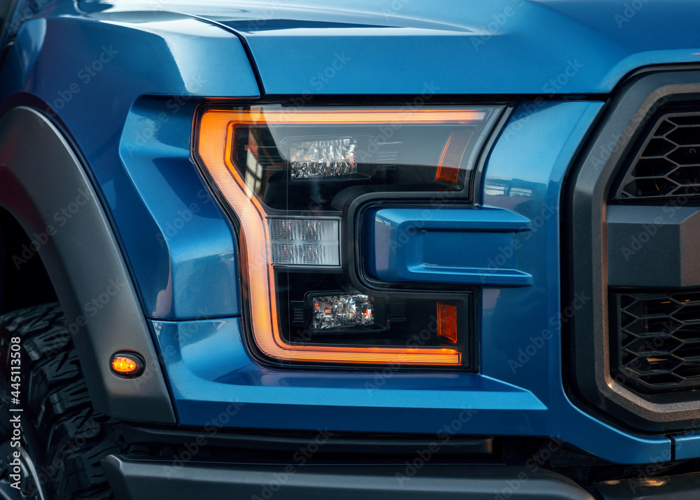 Front illuminated headlights of a blue modern SUV car. Close up detail on one of the LED headlights with flare of modern car