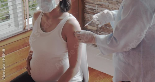 Asian pregnant woman getting COVID-19 coronavirus vaccine at home. Doctor provides vaccine home service to expectant mother. People vaccination and healthcare during home isolation concept.