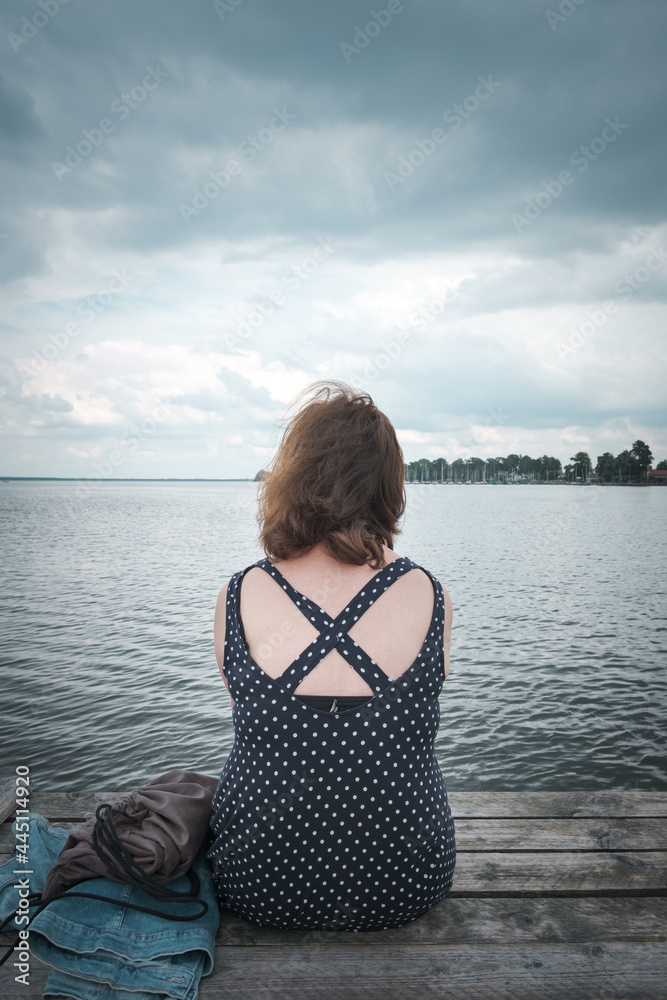 Frau sitzt am Bootsanleger und schaut in die Ferne.Bedeckter Himmel. Frau sitzt am Bootsanleger und schaut in die Ferne.Bedeckter Himmel.