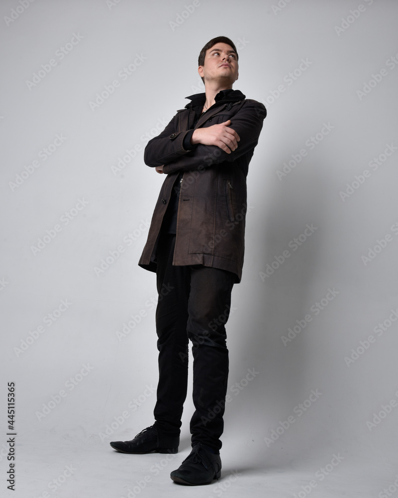 Full length portrait of a brunette man wearing black leather coat. Standing pose isolated against a grey studio background. Full length portrait of a brunette man wearing black leather coat. Standing pose isolated against a grey studio background.