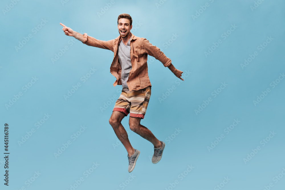 Obraz premium Cool happy man in brown trendy shirt and striped orange and yellow shorts looking into camera, smiling and funny jumping..