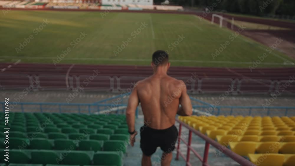 A young muscular man training in the stadium and runs down the steps of the grandstand. Slow motion. Following shot A young muscular man training in the stadium and runs down the steps of the grandstand. Slow motion. Following shot