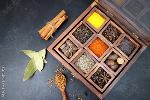 Variety of Indian spices and herbs in a wooden box. Multicolored spices in a wooden organizer, top view. Seasoning background. Bay Leaf, Black Pepper, Cinnamon, Cloves, Coriander, Turmeric, red chili.