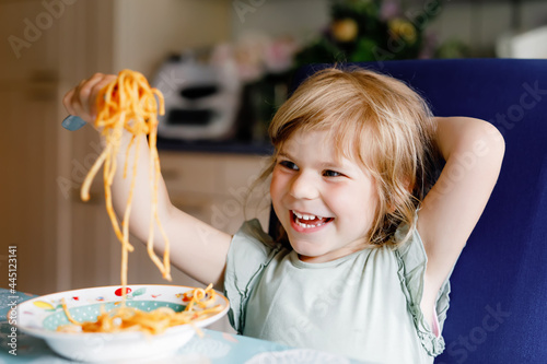 Adorable toddler girl eat pasta spaghetti with tomato bolognese with minced meat. Happy preschool child eating fresh cooked healthy meal with noodles and vegetables at home, indoors.
